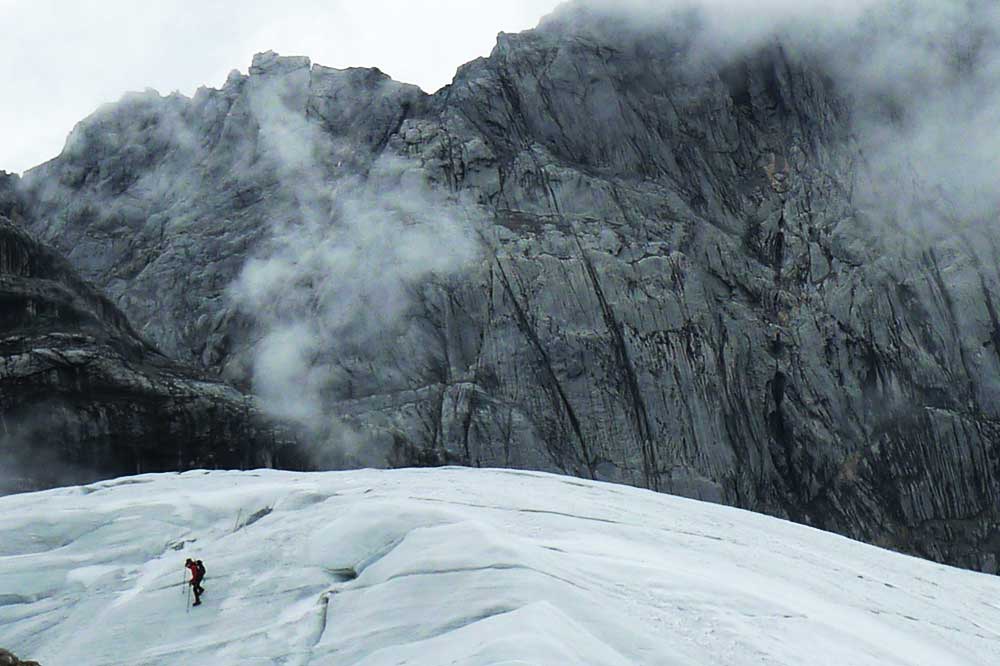 man walking on glacier with carstensz pyramid in background